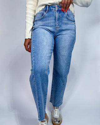 A person wearing light blue high-waisted straight-leg jeans, a white long-sleeve top, and metallic silver sneakers, shown f