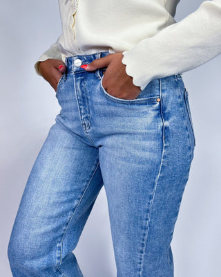A close-up of a person wearing light blue high-waisted denim jeans with a cream-colored long-sleeve top, showing the fro