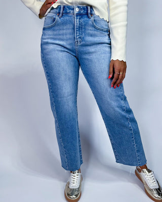 A person wearing light blue high-waisted straight-leg jeans, a white long-sleeve top, and metallic silver sneakers