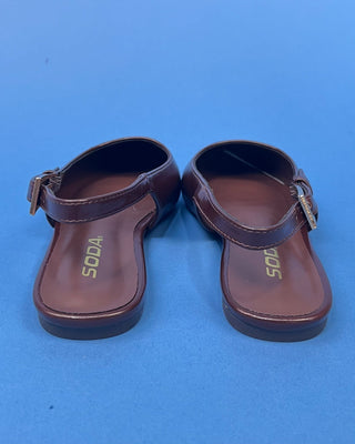 A pair of dark brown leather T-strap sandals with buckle straps and gold 'SODA' branding printed on the soles, shown agai