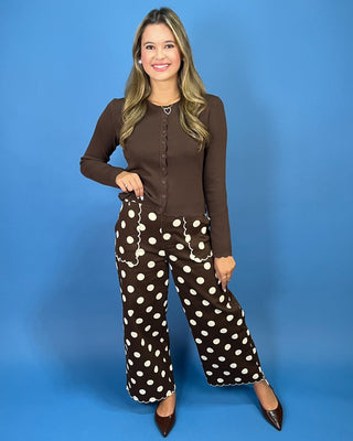 A woman modeling a brown long-sleeve button-front top and matching brown pants with large white polka dots