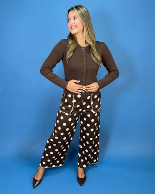 A woman modeling a brown long-sleeve button-front top and matching brown pants with large white polka dots