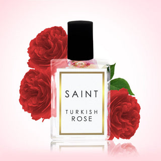 Perfume bottle labeled 'Saint Turkish Rose' surrounded by red roses on a light pink background