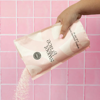 Hand holding a bag of 'sweet grace' mineral soaking salt against a pink tiled background