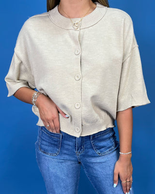 A woman wearing a cream-colored knit cardigan with short sleeves and front buttons, paired with blue jeans