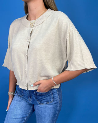 A woman wearing a light beige short-sleeve knit cardigan with a round collar and button front, paired with blue jeans