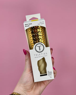 Hand holding a Teleties mini vent brush packaging against a pink background