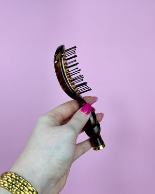 Hand holding a tortoiseshell comb against a pink background