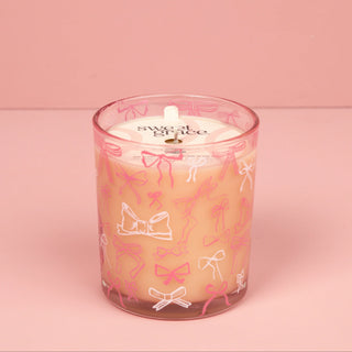 Candle in a glass jar with pink bow designs on a pink background