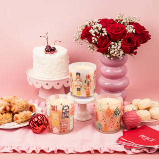 Decorative setup with candles, a cake, and flowers on a pink background